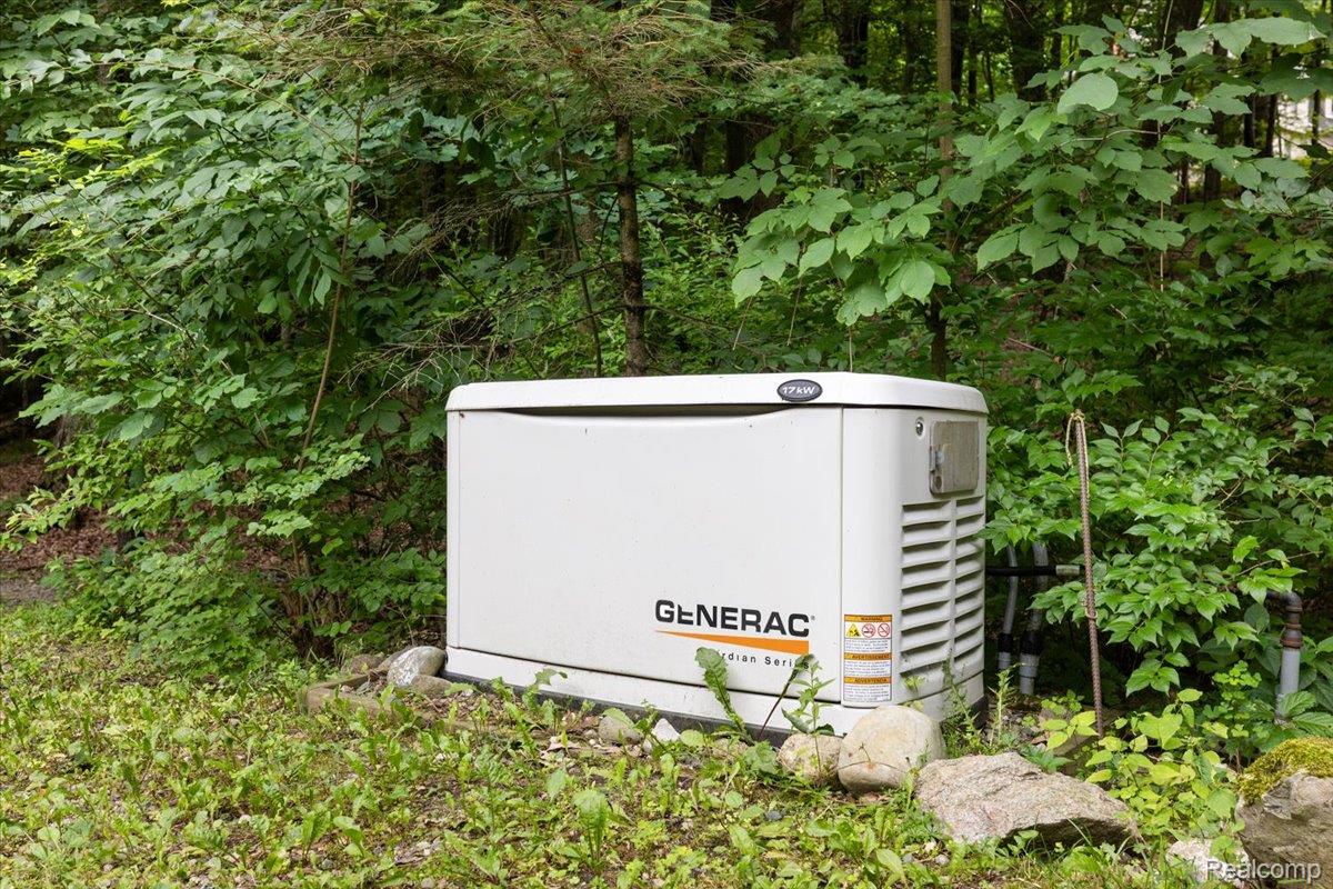 4219 Gardner Road Metamora, MI 48455 - Photo 74 of 84 Freestanding whole-house generator unit on a gravel and rock base, surrounded by natural landscaping and mature trees