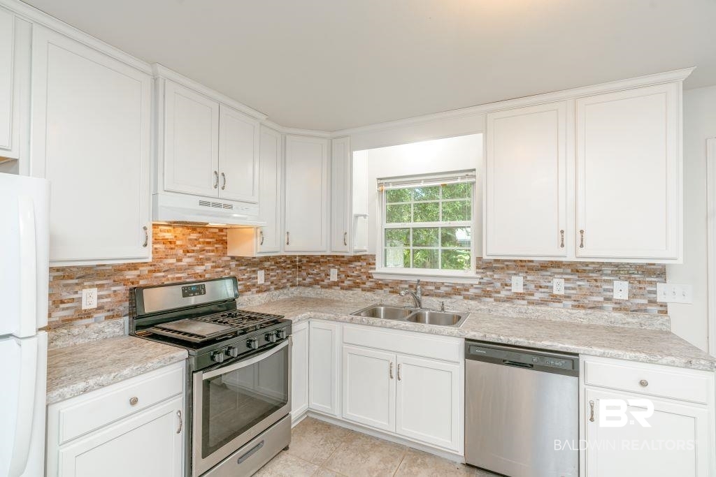 12641 Pecan Street Grand Bay, AL 36541 - Photo 11 of 23 Kitchen with custom exhaust hood, decorative backsplash, sink, appliances with stainless steel finishes, and light tile patterned floors