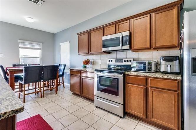 3330 Emerson Road Forney, TX 75126 - Photo 2 of 10 a kitchen with stainless steel appliances granite countertop a stove a sink dishwasher a microwave oven and a dining table with wooden cabinet