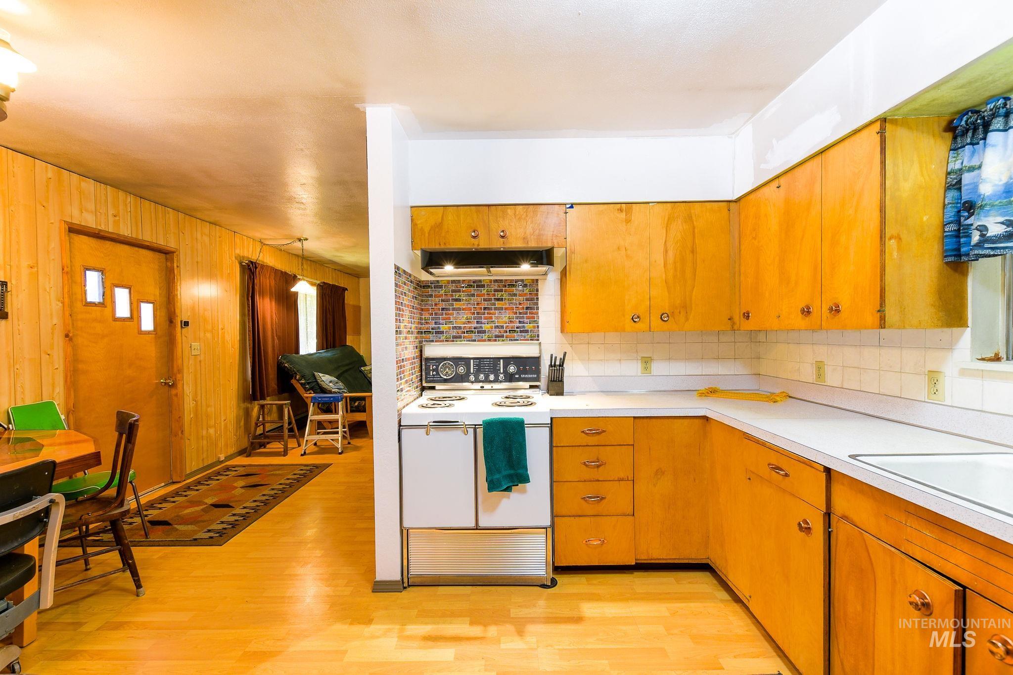 243 North Fir Street Genesee, ID 83832 - Photo 17 of 50 Kitchen featuring white electric range, tasteful backsplash, light countertops, light wood finished floors, and wood walls