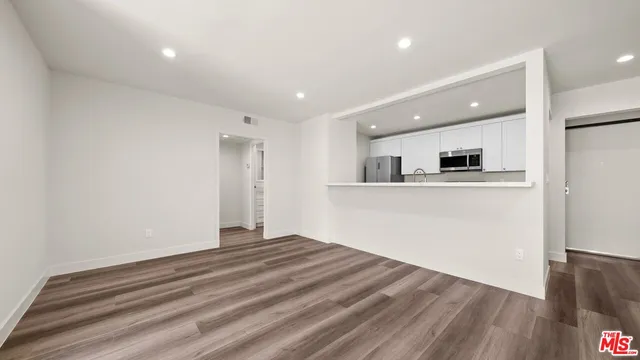 a view of kitchen and empty room with wooden floor