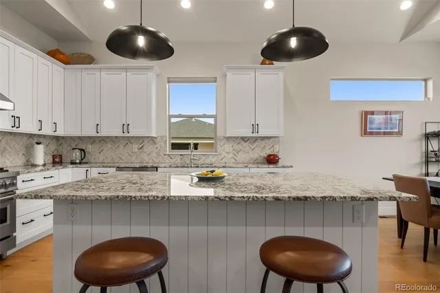 a kitchen with stainless steel appliances granite countertop a sink a stove a dining table and chairs with wooden floor