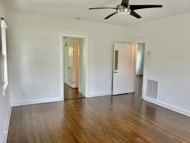 an empty room with wooden floor a ceiling fan and windows