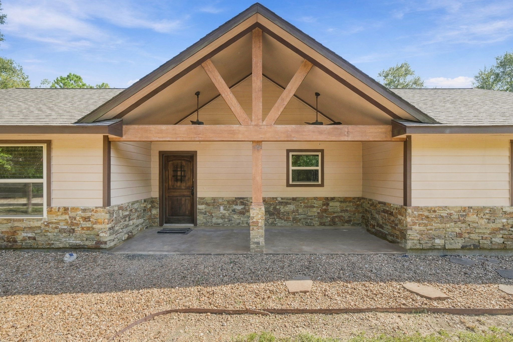7049 Pine Shadows Road Cleveland, TX 77328 - Photo 4 of 49 Charming home with a welcoming front porch, featuring rustic stone accents and a sturdy wooden beam detail under a gabled roof.
