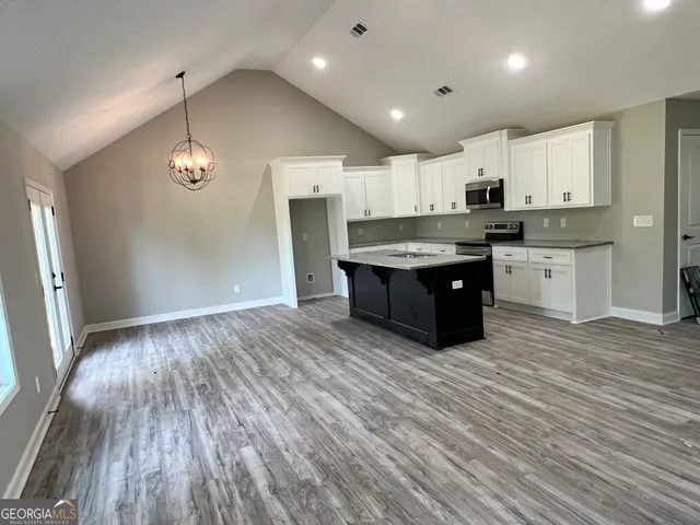 a room with kitchen island stainless steel appliances granite countertop a sink and wooden floor