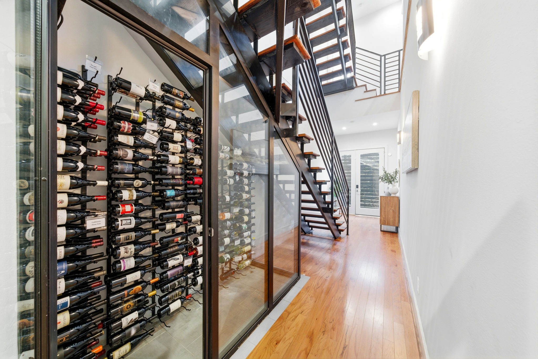 1405 Vermont Street, Unit A Houston, TX 77006 - Photo 3 of 46 A glass-enclosed, climate-controlled wine room serves as a sophisticated focal point beneath the modern floating staircase. This high-capacity wall-mounted display showcases designer finishes and gleaming hardwoods, leading guests through the light-filled hallway toward the first-floor guest suite.