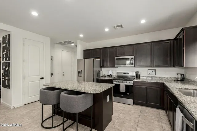a kitchen with stainless steel appliances granite countertop a sink a stove a refrigerator cabinets and a dining table