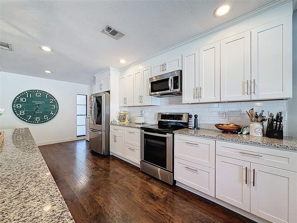 7813 River Ridge Drive Temple Terrace, FL 33637 - Photo 17 of 43 a kitchen with stainless steel appliances granite countertop white cabinets a sink a stove a refrigerator and microwave with wooden floor