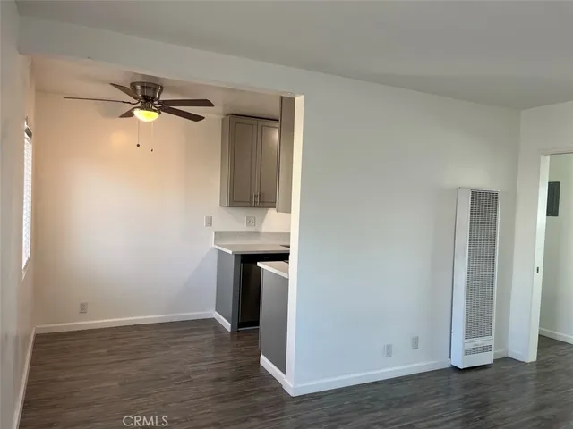 an empty room with wooden floor a ceiling fan and kitchen view