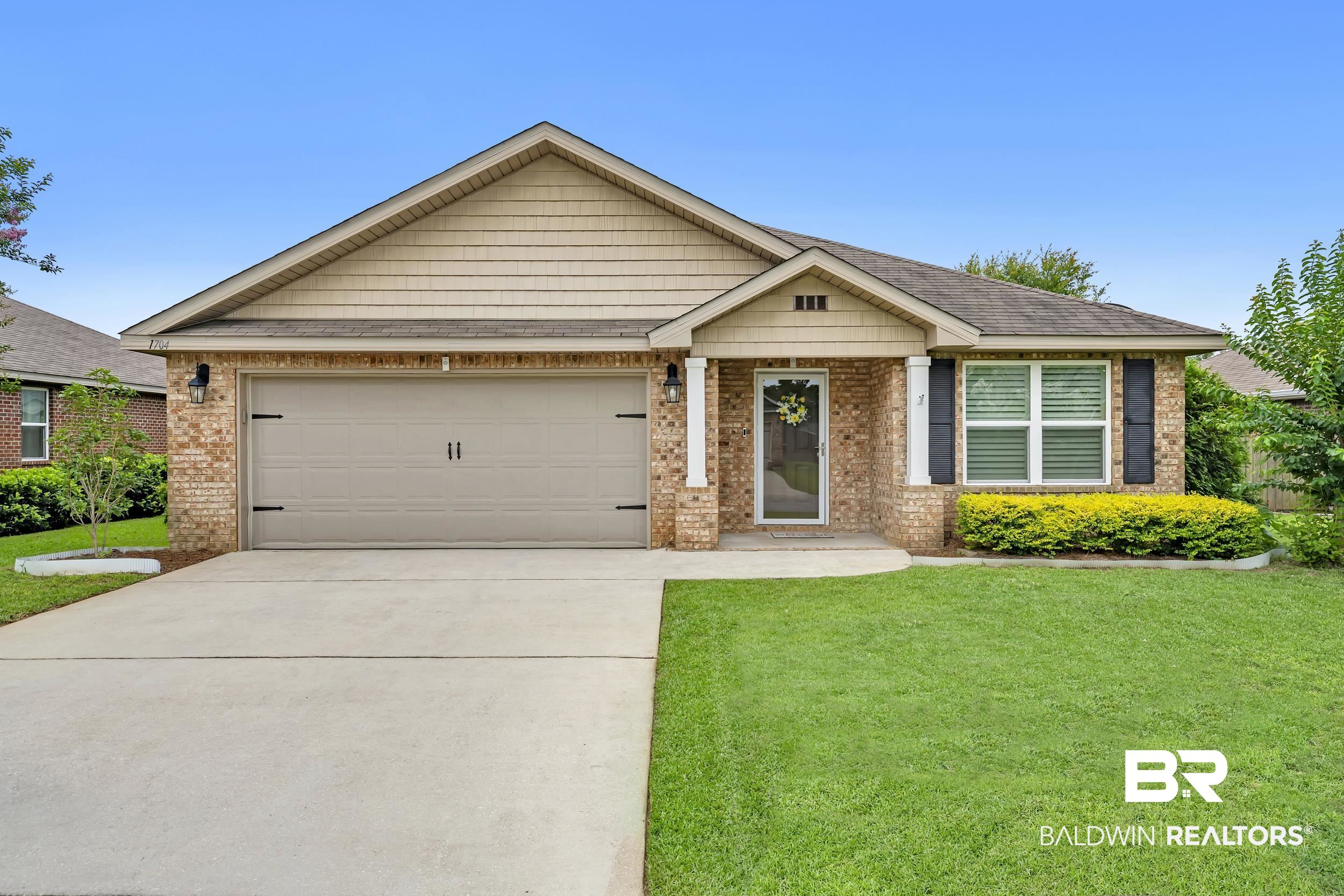 1704 Abbey Loop Foley, AL 36535 - Photo 1 of 38 Brick and siding exterior featuring a covered entry porch with white columns, a two-car garage, a concrete driveway, and a front lawn with established landscaping