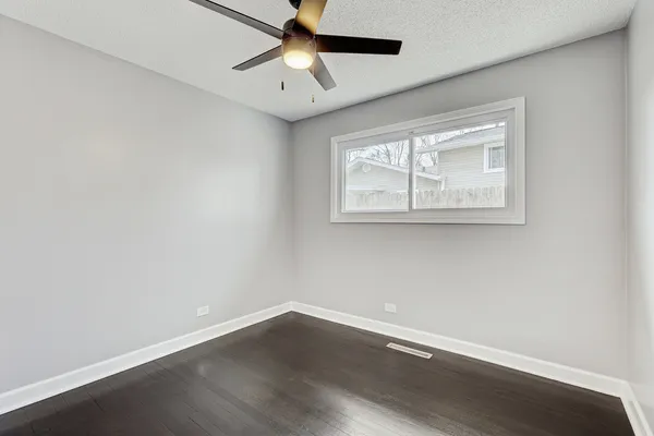 an empty room with wooden floor chandelier fan and windows