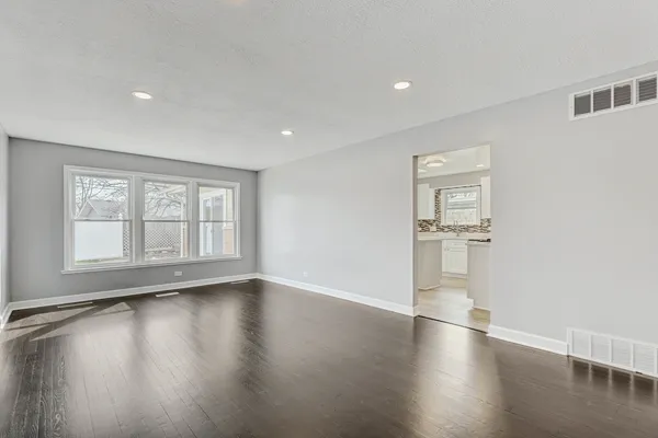 a view of empty room with wooden floor and kitchen view