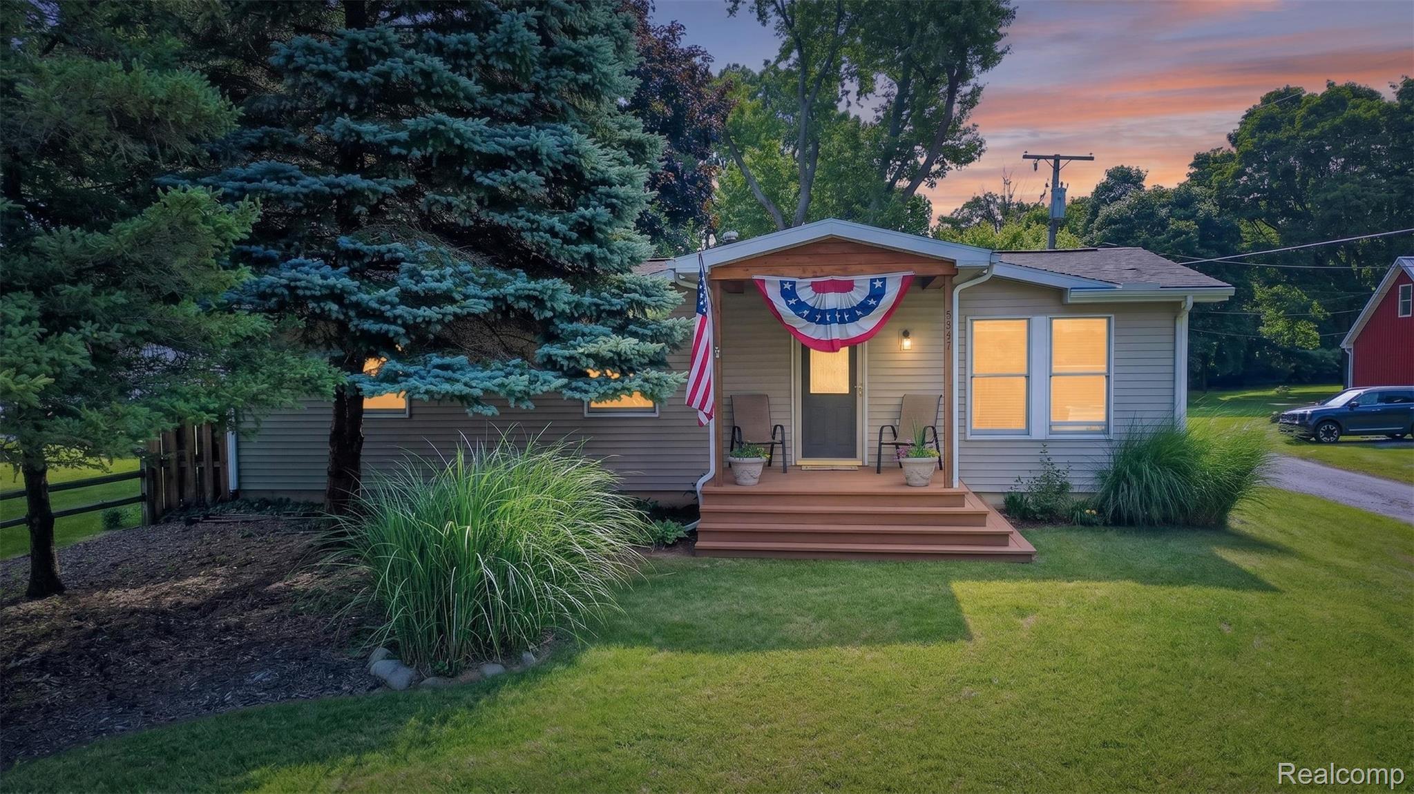 5977 Anglers Road Ortonville, MI 48462 - Photo 63 of 63 Front facade featuring horizontal siding, a covered porch with wood-finish decking, and mature landscaping including evergreen trees