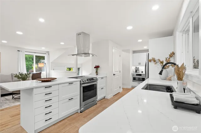 a large white kitchen with stainless steel appliances a stove a chimney a sink and dishwasher