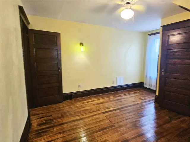 a view of an empty room with wooden floor and fan