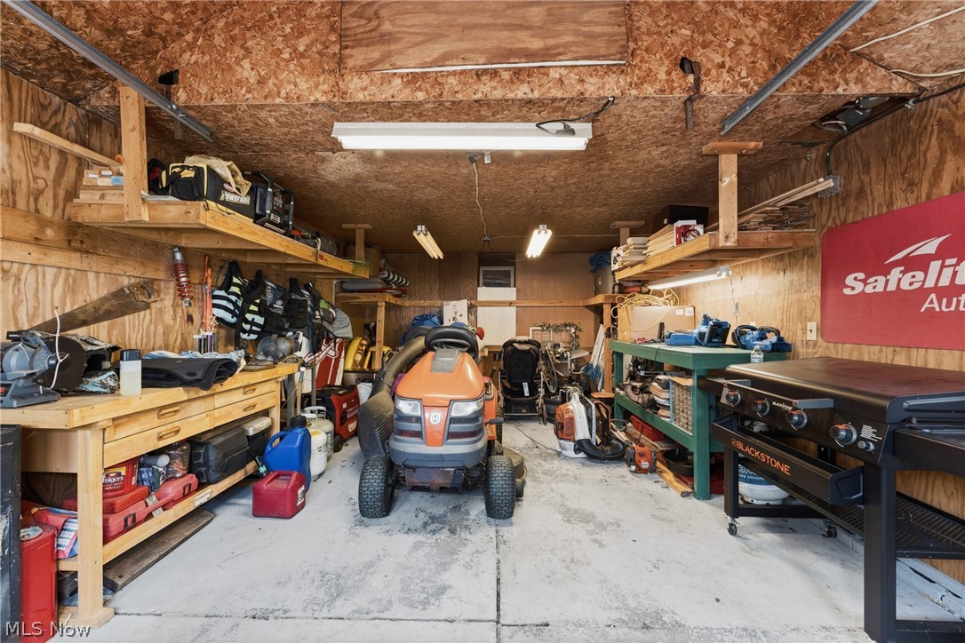 258 Randolph Road Mogadore, OH 44260 - Photo 30 of 49 Garage interior featuring a concrete floor, plywood paneling, built-in shelving, a workbench, and fluorescent lighting