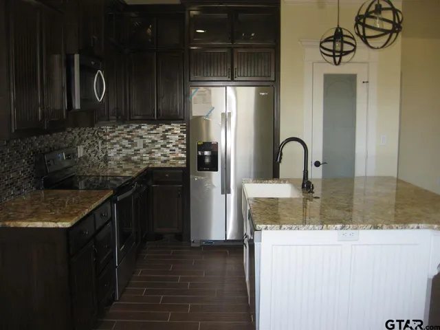 a kitchen with kitchen island granite countertop a refrigerator and a sink