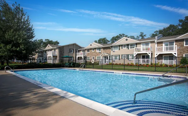 a view of a white house with a large pool and lawn chairs under an umbrella