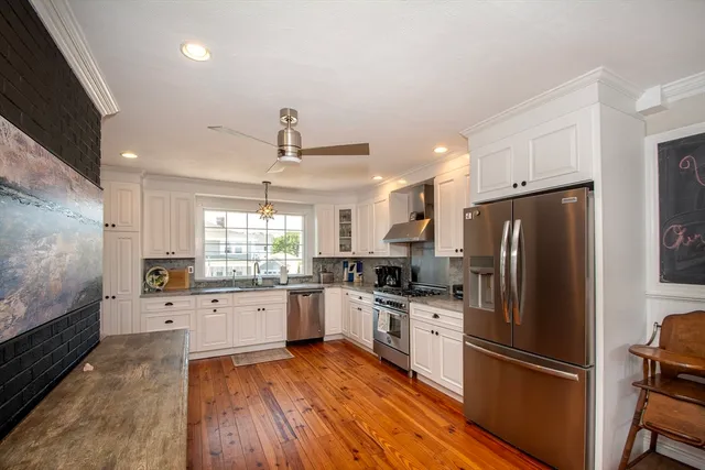 a kitchen with granite countertop a refrigerator a sink dishwasher a stove and white cabinets with wooden floor