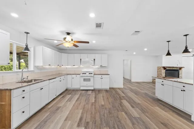 a large kitchen with granite countertop a large center island a sink dishwasher and a stove with wooden floor