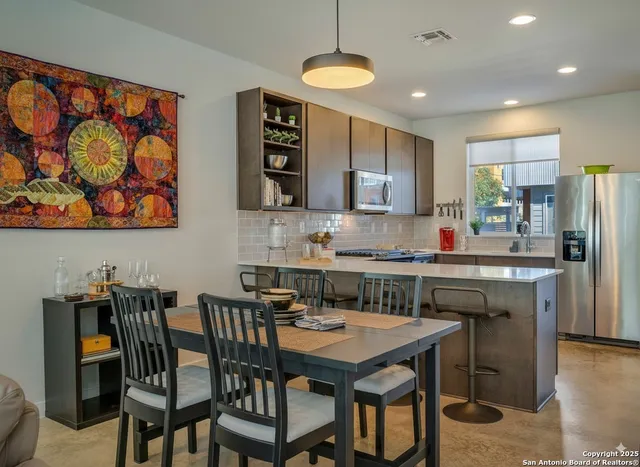 a kitchen with stainless steel appliances granite countertop a dining table chairs refrigerator and cabinets