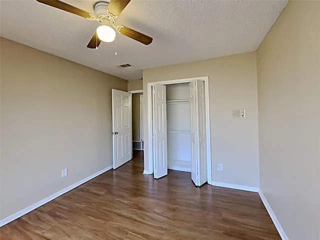 an empty room with wooden floor chandelier fan and closet area with wooden floor