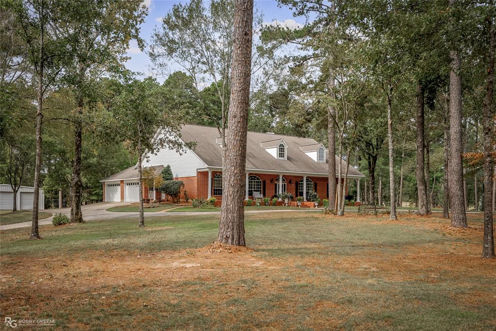 New england style home featuring covered porch, roof with shingles, brick siding, a front yard, and driveway