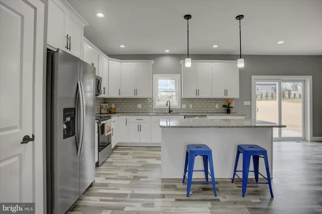 a kitchen with stainless steel appliances granite countertop a refrigerator a sink dishwasher a stove and white cabinets with wooden floor