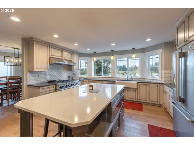a kitchen with stainless steel appliances granite countertop a sink a stove a refrigerator cabinets and a dining table