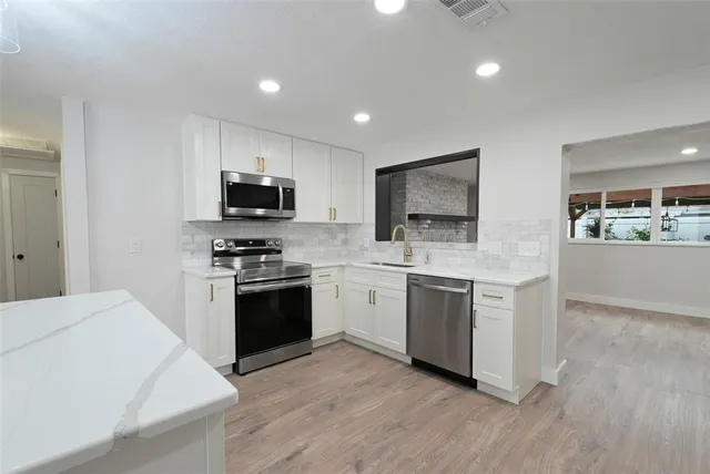 a kitchen with stainless steel appliances granite countertop a stove top oven a sink dishwasher a refrigerator and a microwave oven with wooden floor