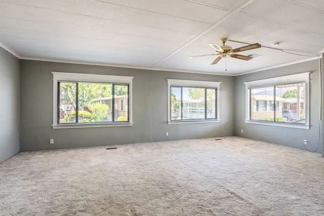 a view of an empty room with windows and chandelier fan
