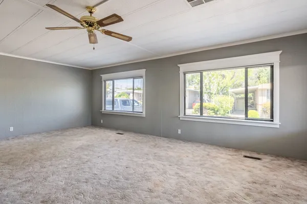 an empty room with chandelier fan and windows