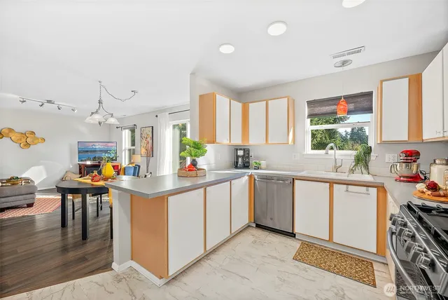 a kitchen with stainless steel appliances kitchen island granite countertop a stove a sink dishwasher and white cabinets with wooden floor