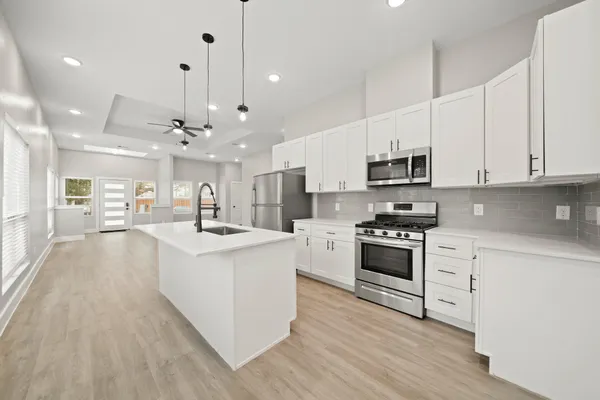 a large white kitchen with lots of counter space a sink appliances and cabinets