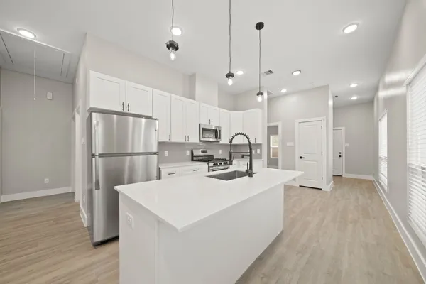 a kitchen with stainless steel appliances a refrigerator a sink dishwasher a stove and white cabinets with wooden floor