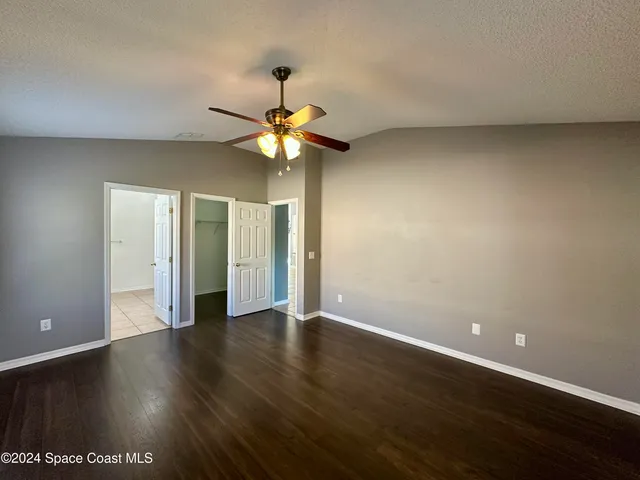 an empty room with wooden floor chandelier fan and windows