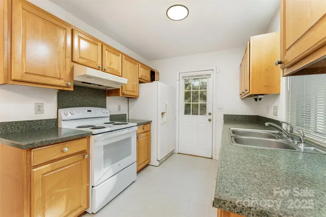 a view of an empty room with window a kitchen and wooden floor