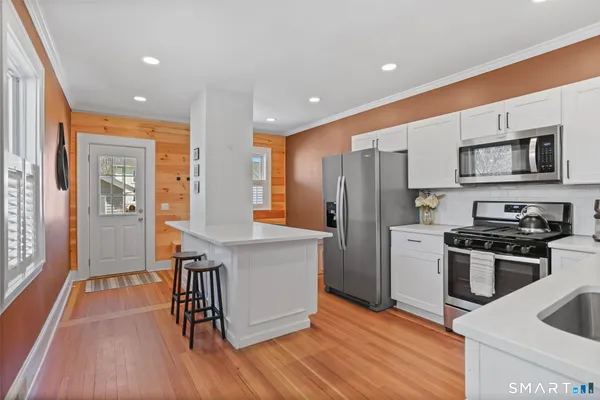 a kitchen with stainless steel appliances granite countertop a refrigerator a stove top oven and a sink with wooden floor