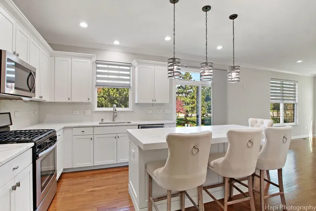 a kitchen with stainless steel appliances granite countertop a stove top oven a sink dishwasher a dining table and chairs with wooden floor