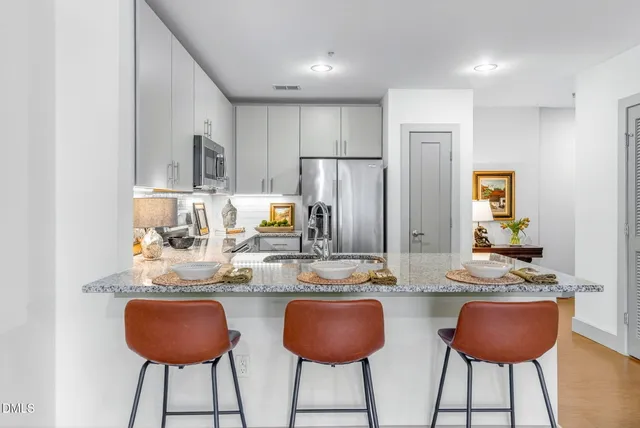 a kitchen with stainless steel appliances granite countertop a dining table chairs and a refrigerator