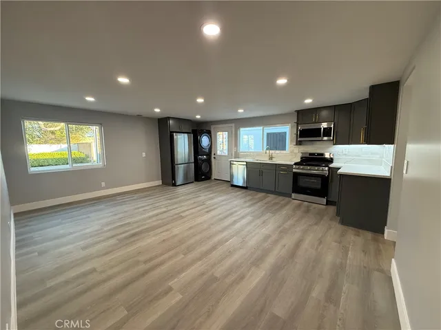 a view of kitchen with stainless steel appliances granite countertop a refrigerator a sink dishwasher a stove and a refrigerator with wooden floor