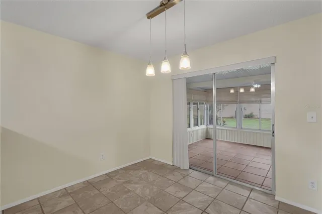 an empty room with kitchen view and a chandelier fan