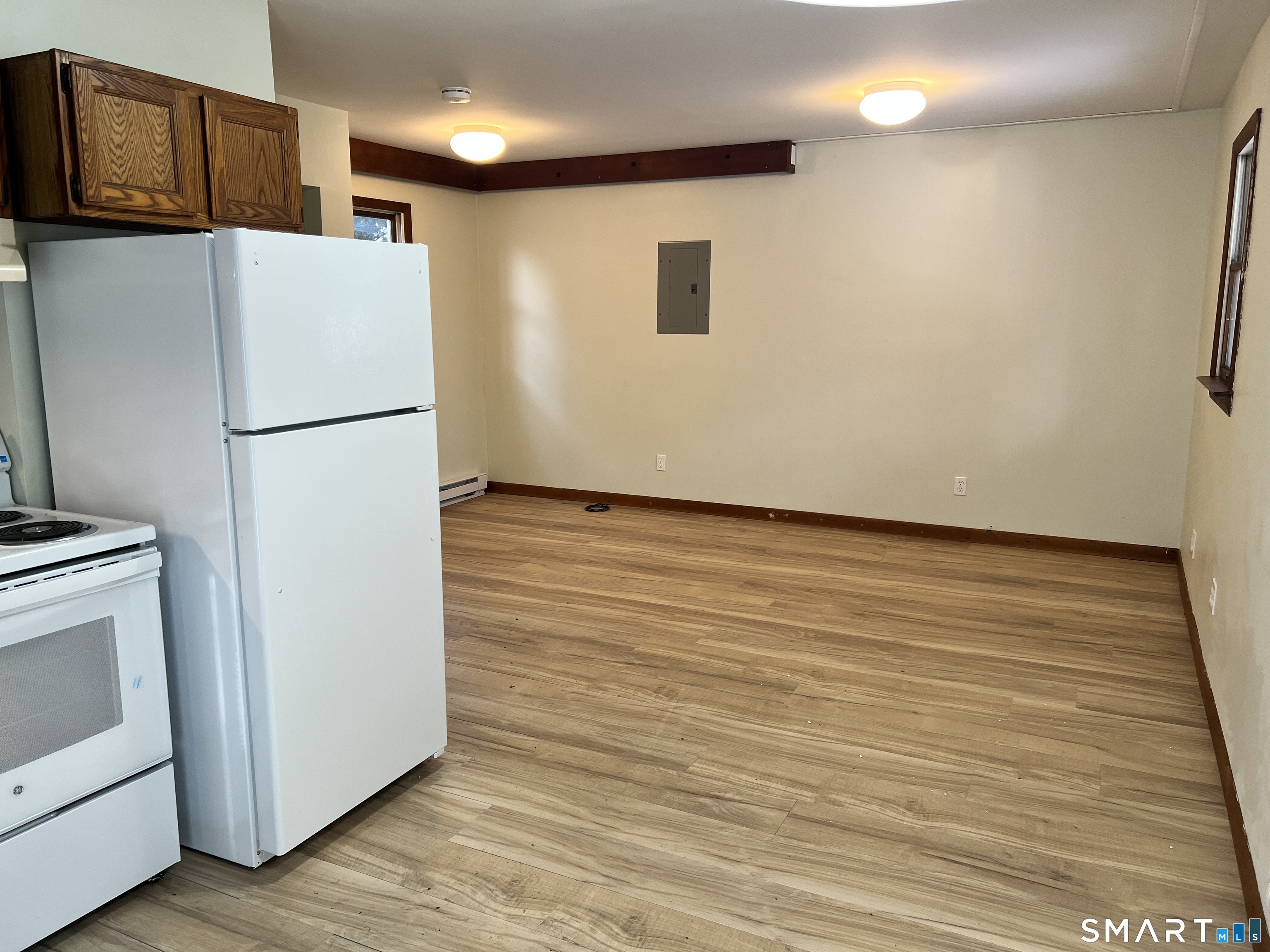 a view of a refrigerator in kitchen and an empty room with wooden floor