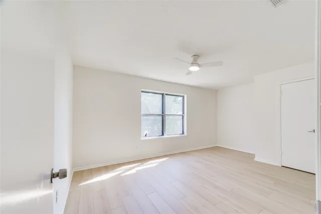 an empty room with wooden floor ceiling fan and windows