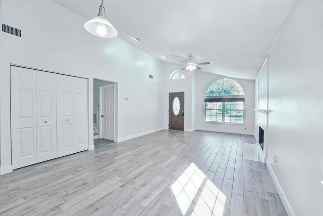 an empty room with wooden floor fan and windows