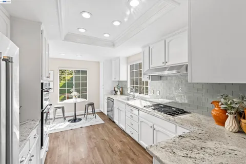 a kitchen with stainless steel appliances granite countertop a stove a sink a refrigerator and white cabinets with wooden floor