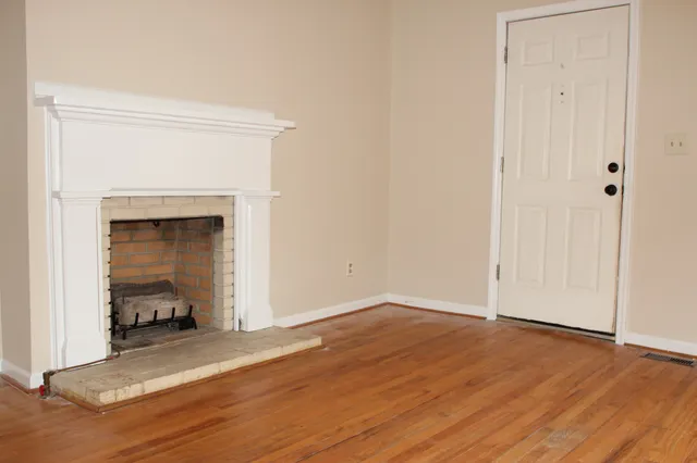 a view of an empty room with wooden floor and a fireplace