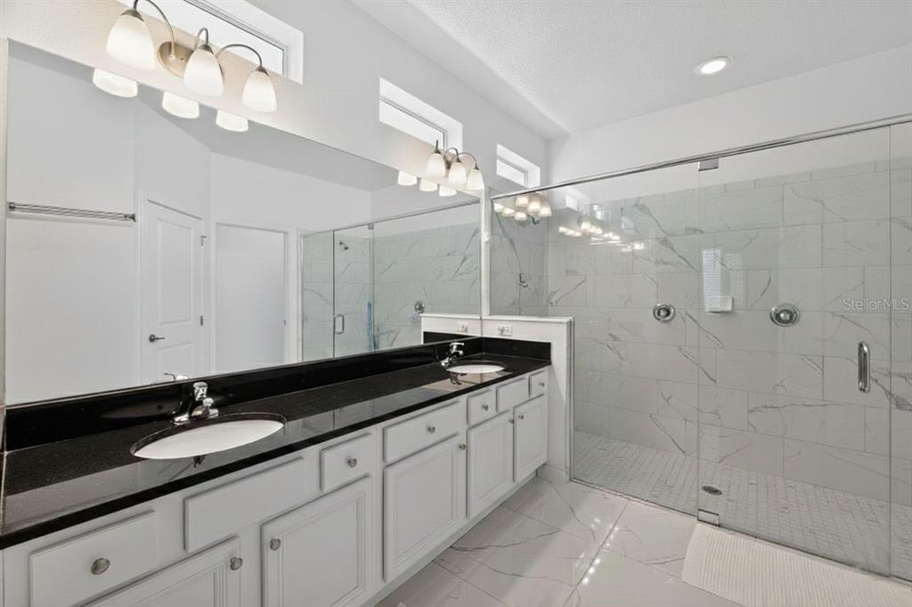 4577 Cabello Loop Kissimmee, FL 34746 - Photo 16 of 37 a spacious bathroom with a granite countertop sink a mirror and a shower