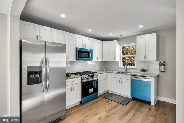 a kitchen with stainless steel appliances granite countertop a refrigerator a sink dishwasher a stove and white cabinets with wooden floor