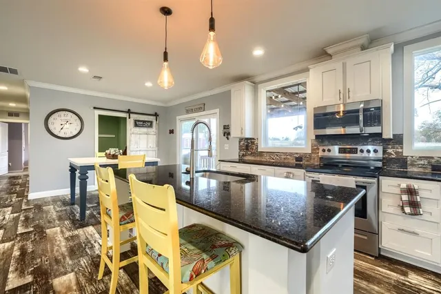 a kitchen with stainless steel appliances granite countertop a sink dishwasher a flat tv screen and a dining table with wooden floor